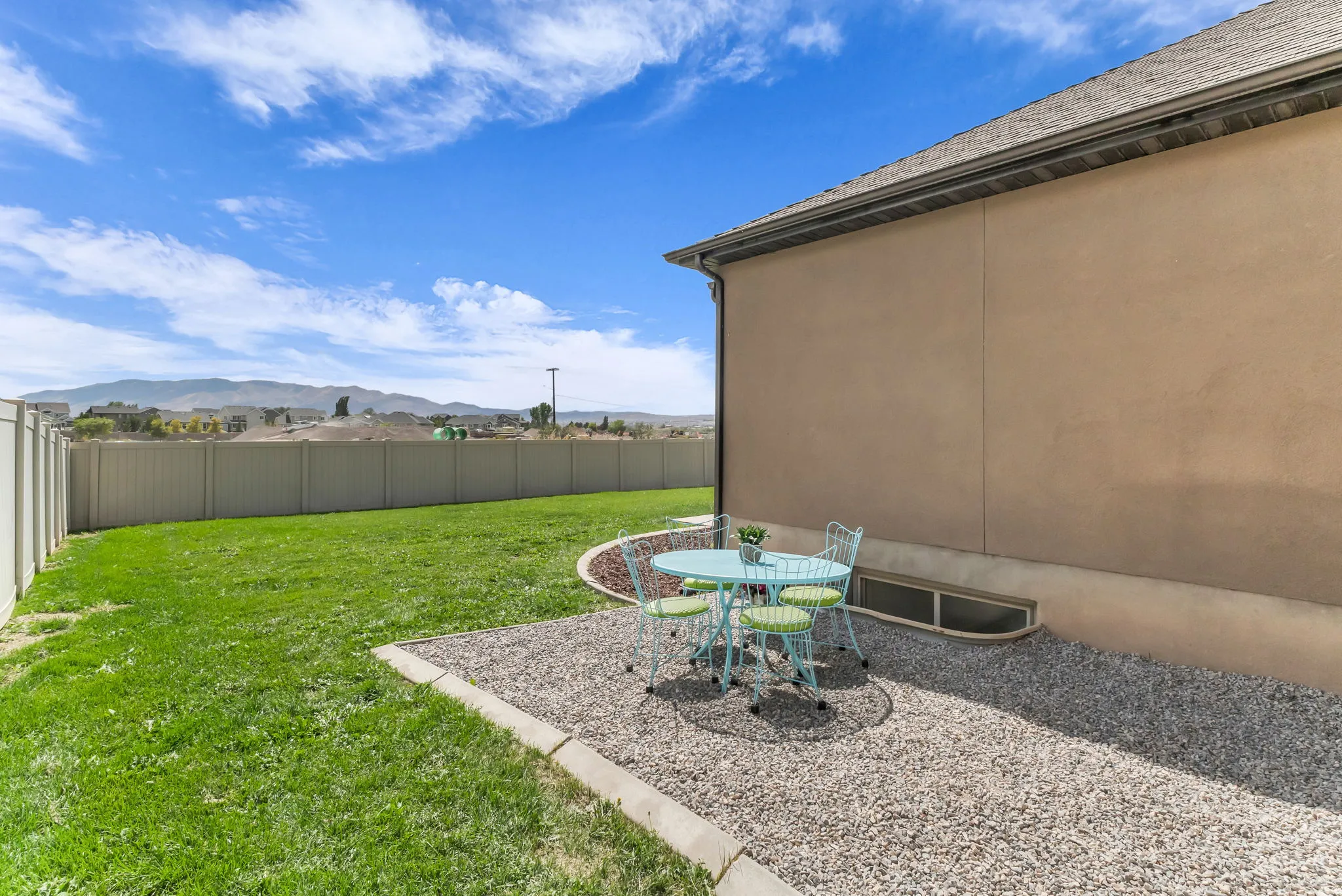 Expansive backyard featuring a green lawn, gravel patio area, perimeter fencing, and distant mountain scenery