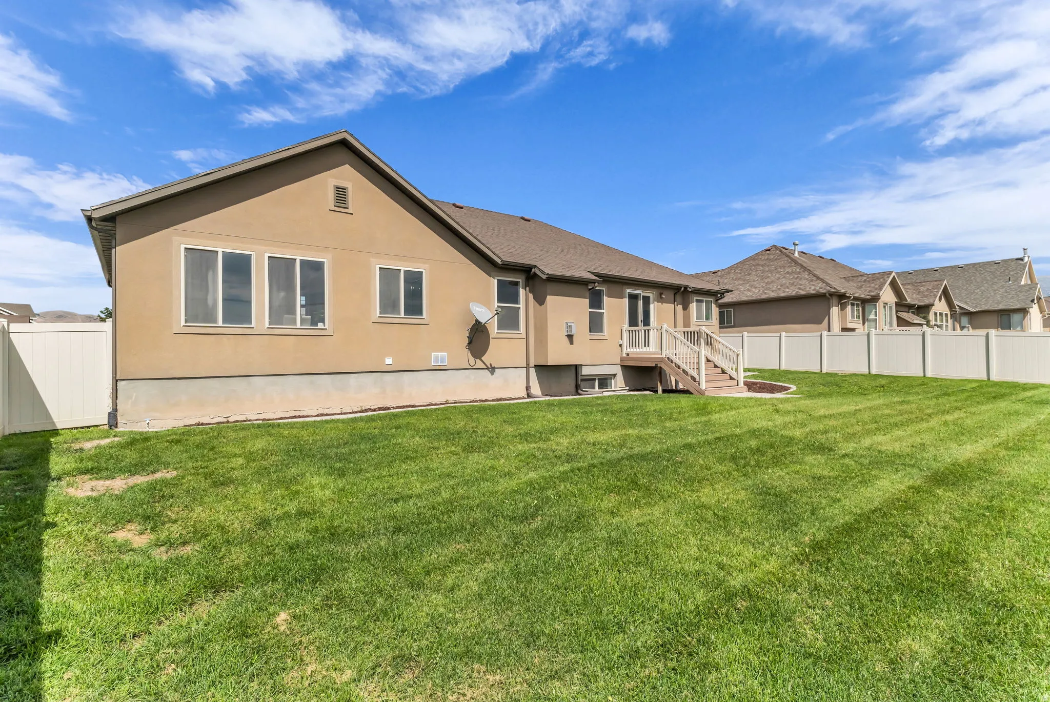 Expansive backyard with a manicured lawn, full vinyl fencing, and a private deck with stairs