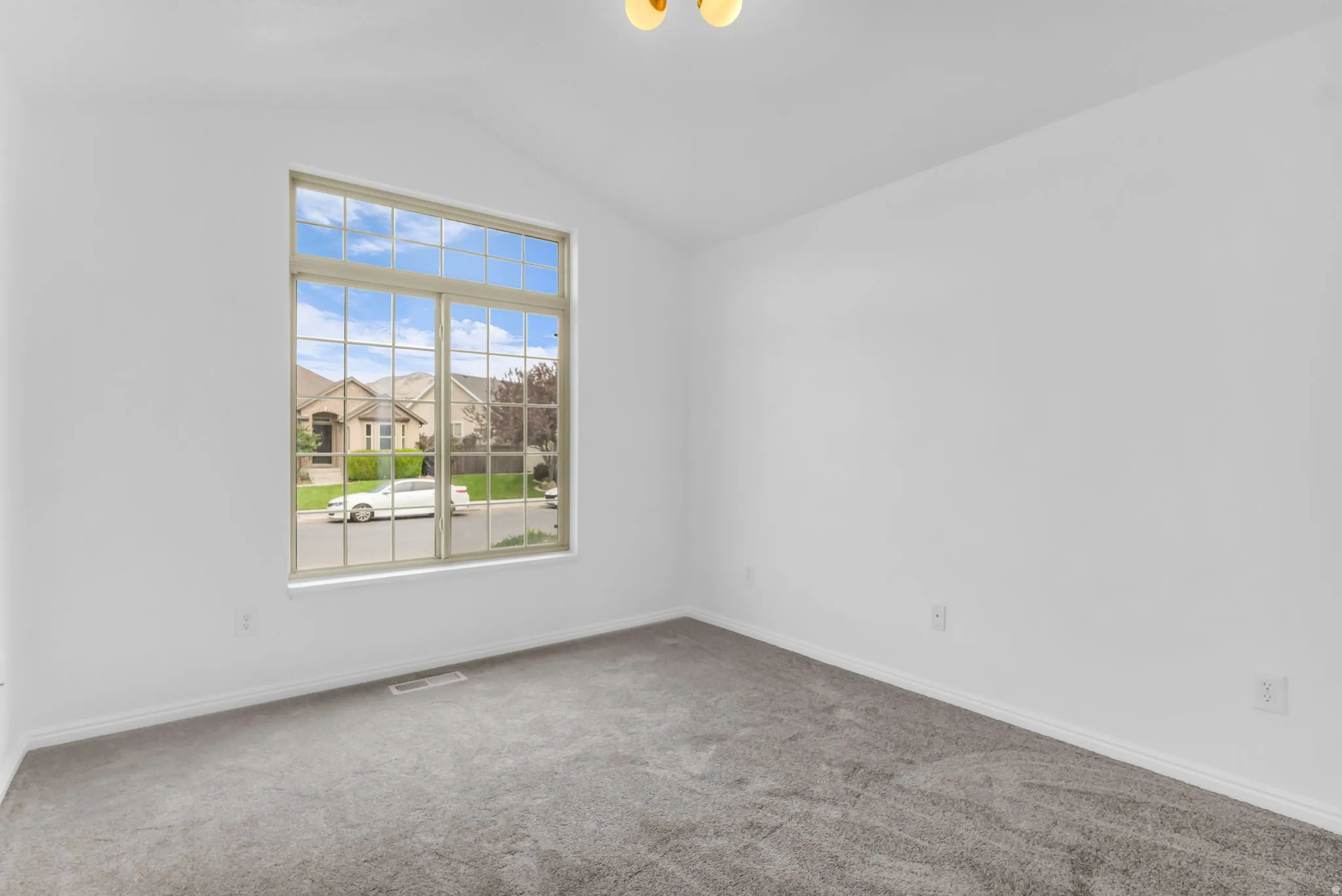 Vaulted ceiling with an overhead light fixture, large multi-pane window, and carpet flooring