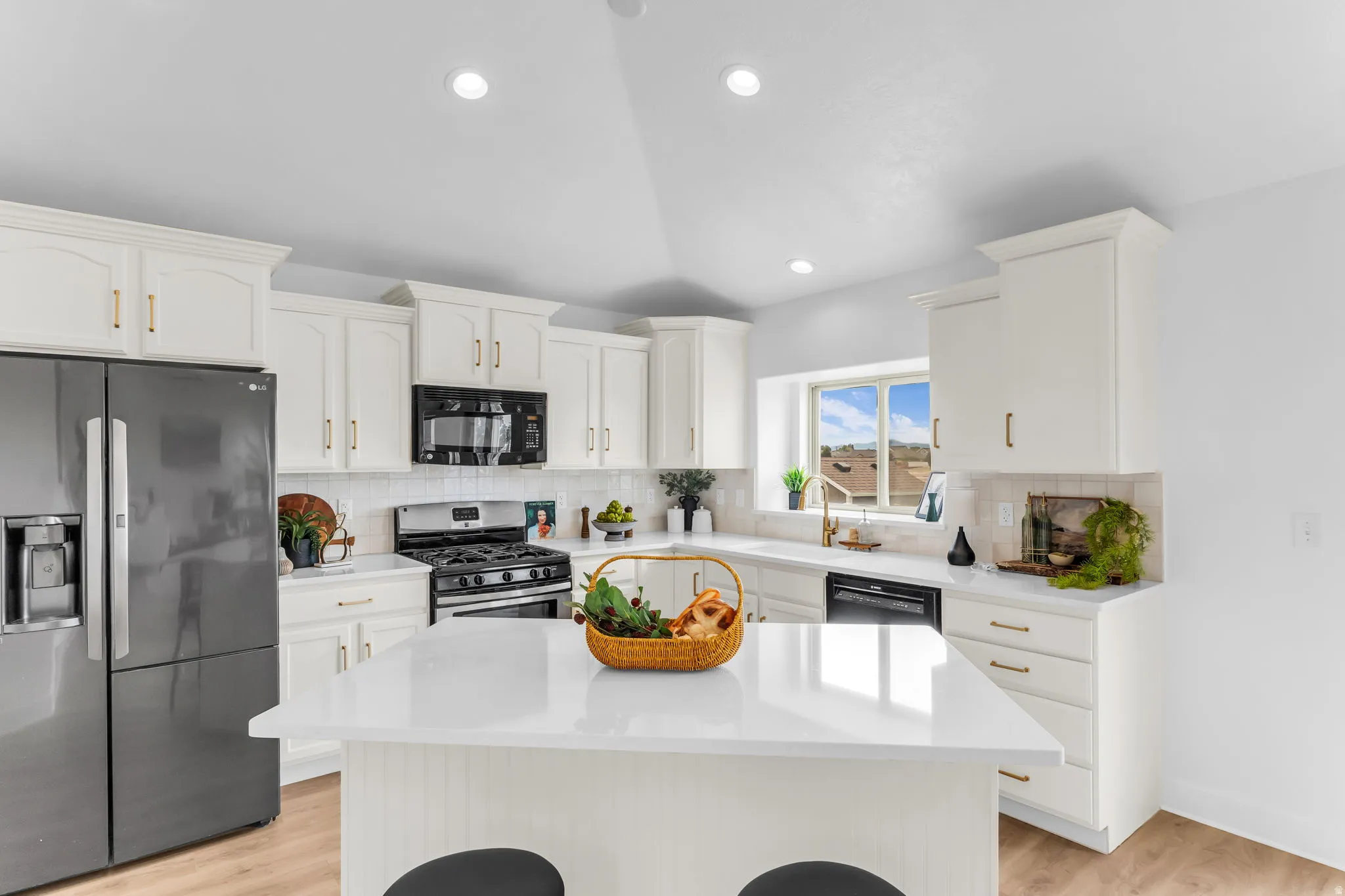 White cabinetry with gold-tone hardware, stainless steel appliances, white subway tile backsplash, and light-tone wood-finish flooring