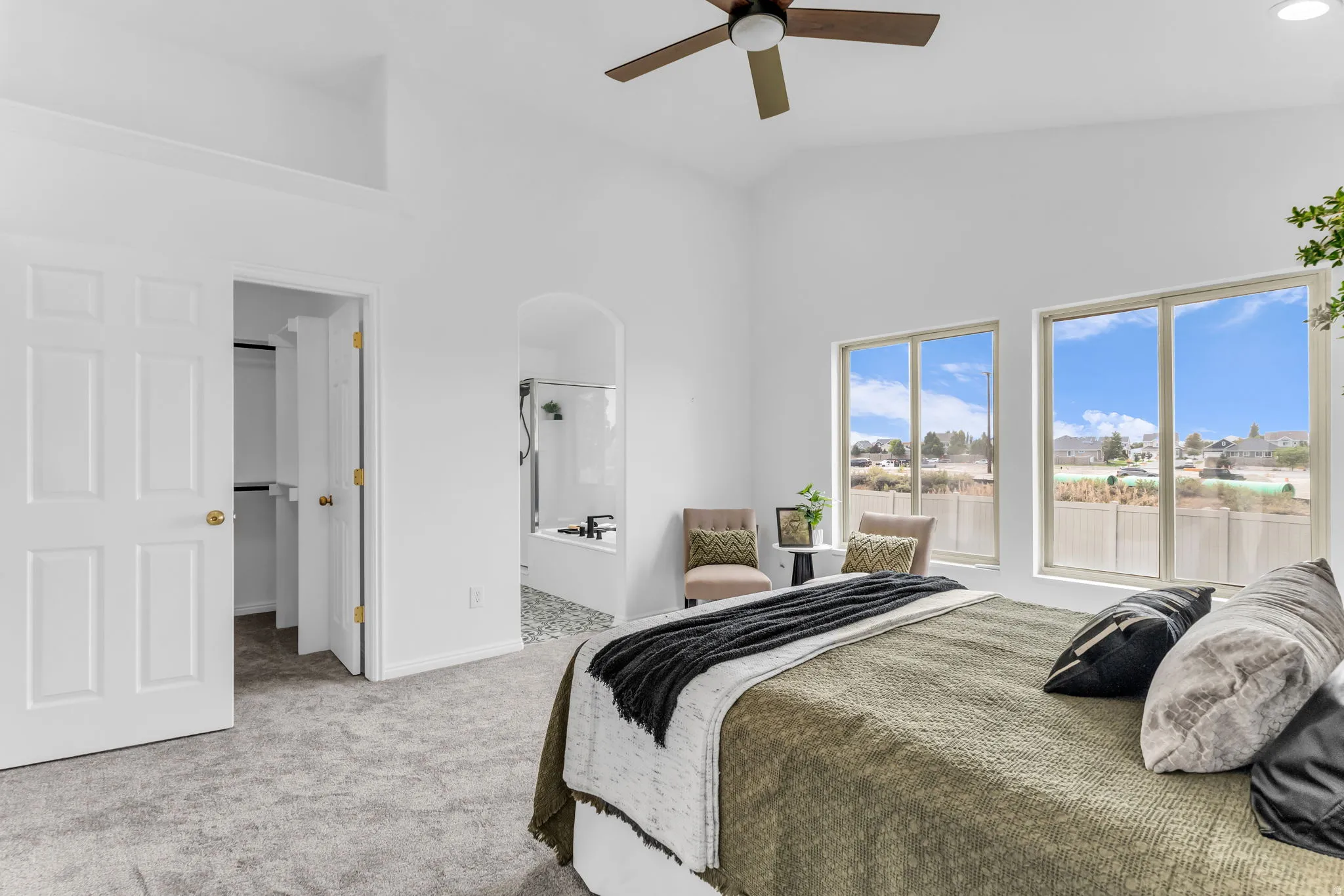 High ceilings with a ceiling fan, plush carpeting, two large windows, an arched doorway to a tiled bathroom, and a walk-in closet with double doors