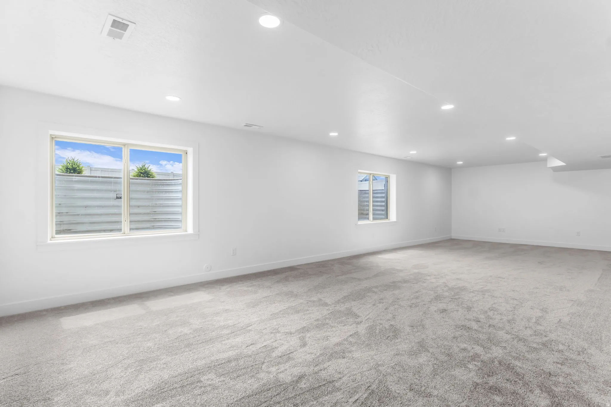 Spacious room with plush gray carpeting, recessed ceiling lighting, and multiple windows