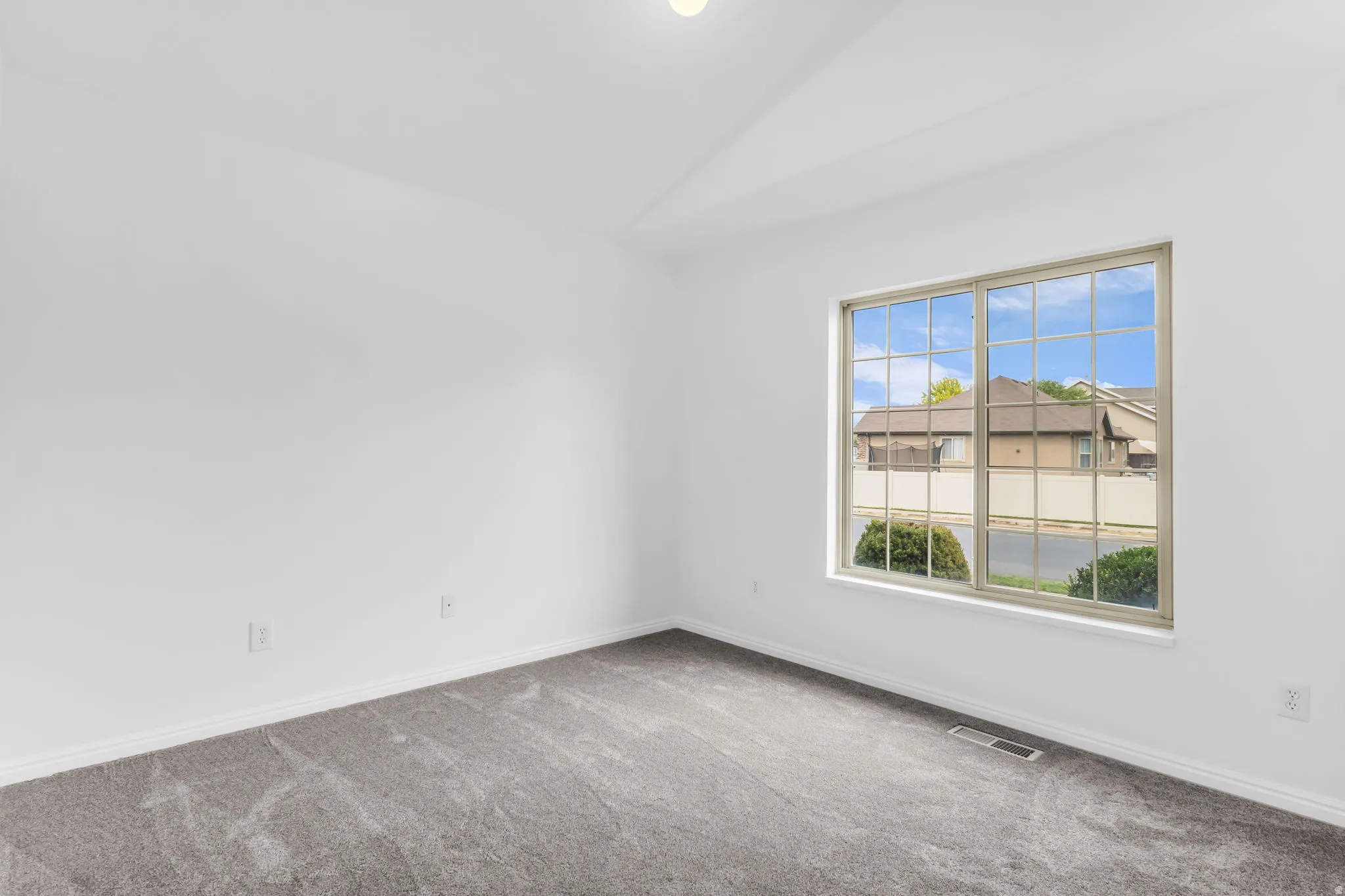 Neutral wall paint with sloped ceiling, gray carpeting, and a grid-pattern window