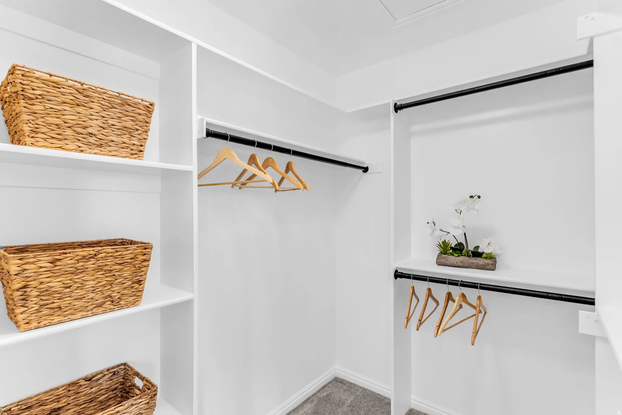 Built-in closet shelving, multiple hanging rods with matte black finish, and gray carpet flooring