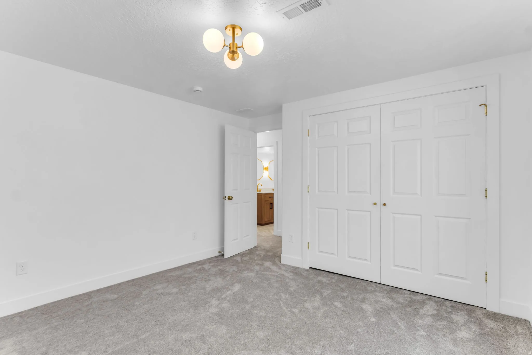 Plush gray carpeting, white painted walls, and a modern gold-finish ceiling light fixture