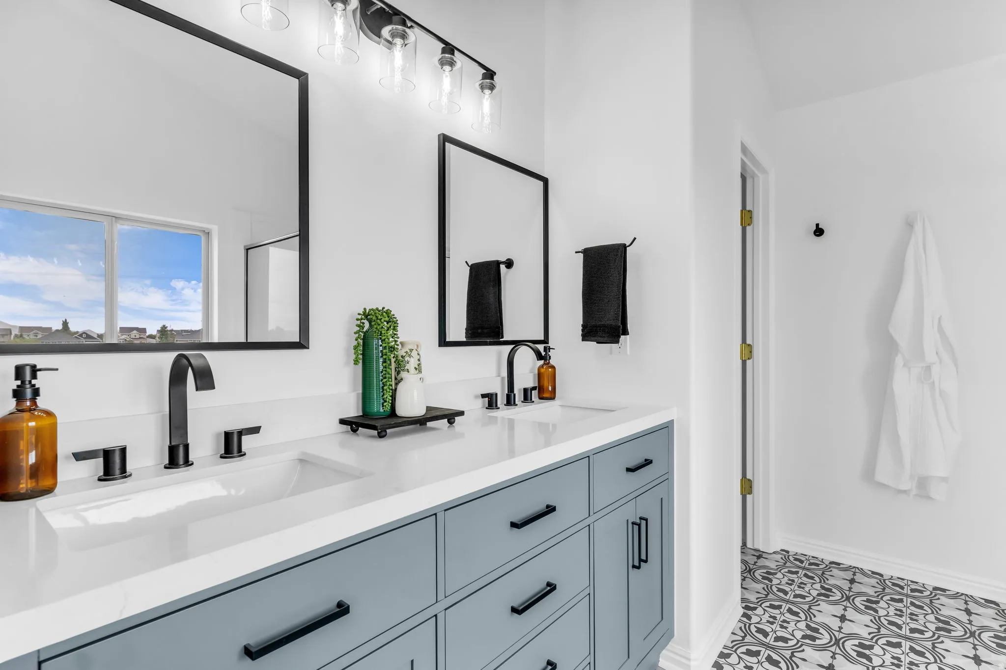 Dual vanity with integrated sinks, matte black fixtures, framed mirrors, and a decorative tile floor