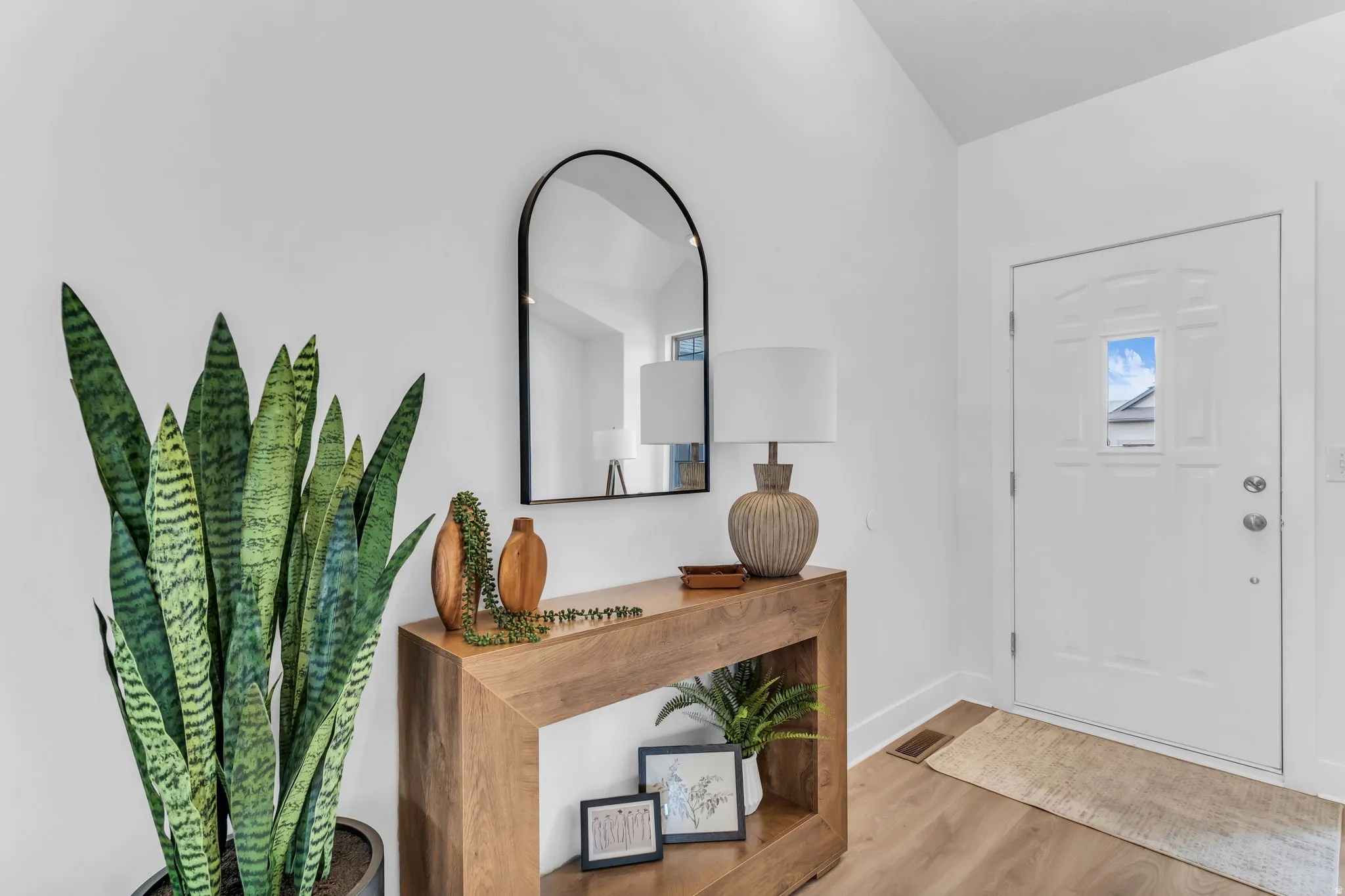 White paneled entry door with frosted glass insert, wood-finish flooring, and a vaulted ceiling