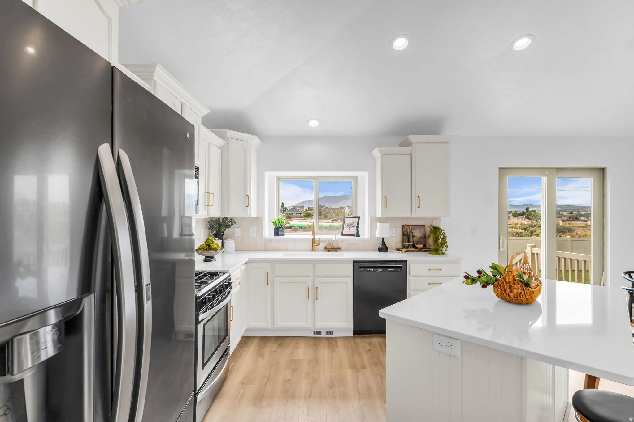 Kitchen featuring white cabinetry with gold-finish hardware, stainless steel and black appliances, light-toned wood-finish flooring, and a sliding glass door to an outdoor deck