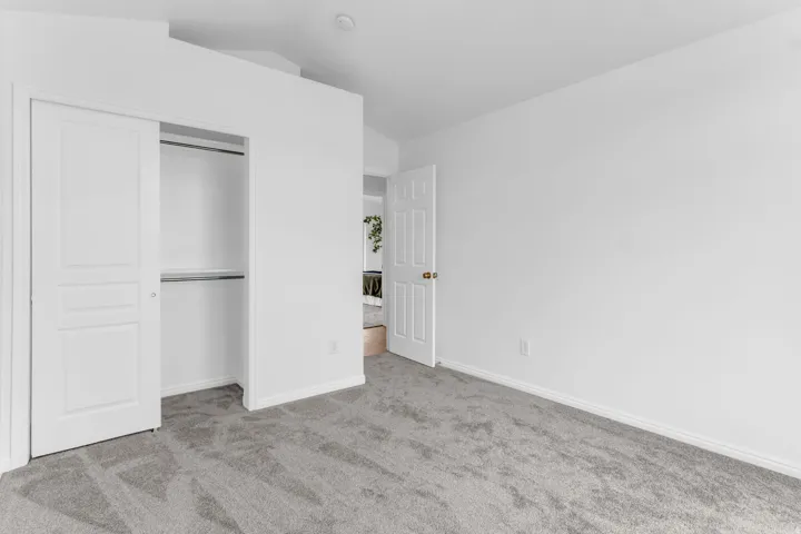 White interior walls, gray carpet flooring, recessed ceiling lighting, a built-in closet with sliding panel doors, and a paneled interior door with brass hardware