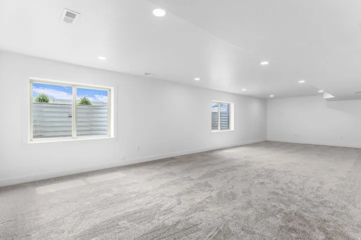 Spacious room with plush gray carpeting, recessed ceiling lighting, and multiple windows