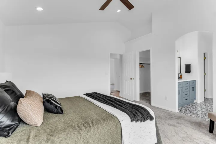 Vaulted ceiling with recessed lighting, ceiling fan, carpet flooring, arched doorway, and a vanity with a rectangular sink
