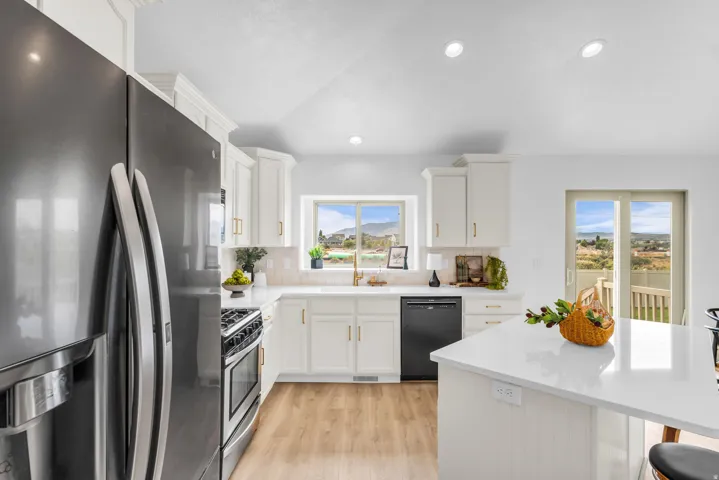 Kitchen featuring white cabinetry with gold-finish hardware, stainless steel and black appliances, light-toned wood-finish flooring, and a sliding glass door to an outdoor deck