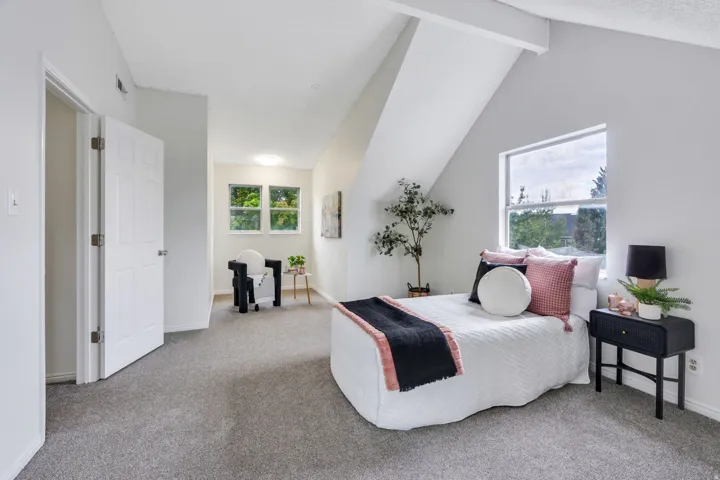 Sloped ceiling with exposed beams, dual windows, gray carpeting, and white paneled door