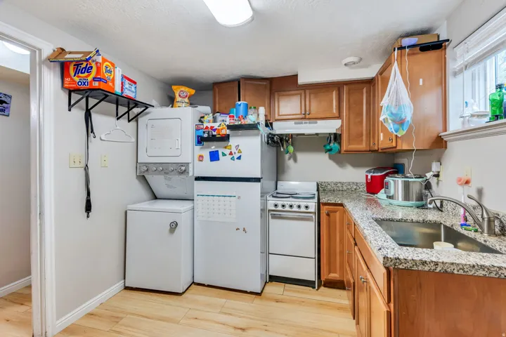 Compact kitchen area featuring wood-finish flooring, granite-style countertops, wood cabinetry, a stainless steel sink, and a window for natural light