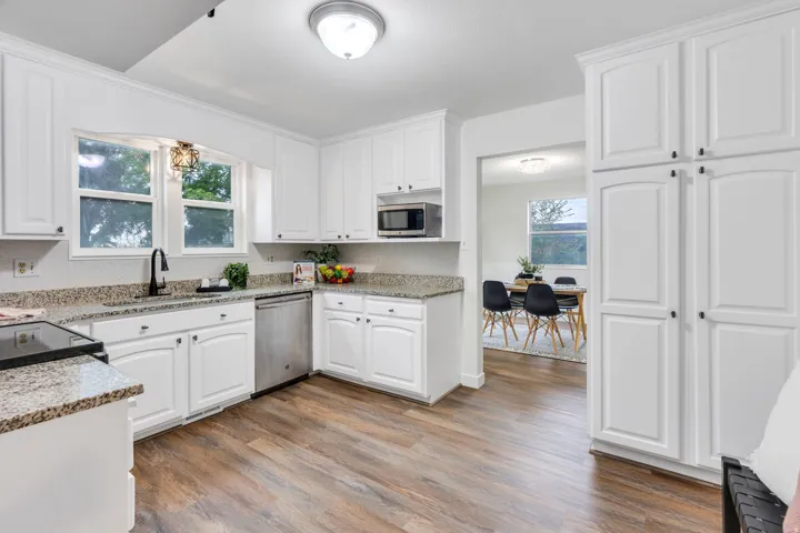 Kitchen featuring white cabinetry, speckled countertops, wood-finish flooring, stainless steel appliances, and a pass-through to an adjacent room