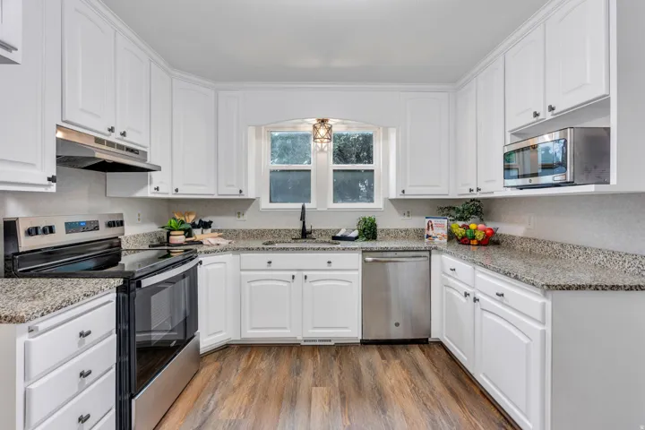 White cabinetry with dark hardware, stone-finish countertops, stainless steel appliances, wood-finish flooring, and a built-in microwave