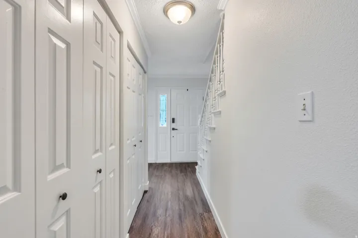 Entryway featuring wood-finish flooring, white paneled bifold doors, a double entry door with decorative glass inserts, and a staircase with white balusters
