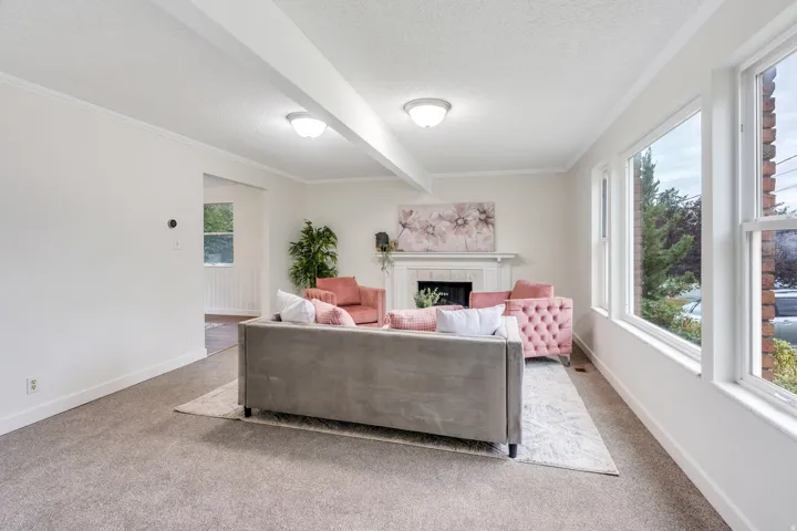 Carpeted living area featuring a decorative fireplace with a mantel, multiple large windows, and overhead lighting