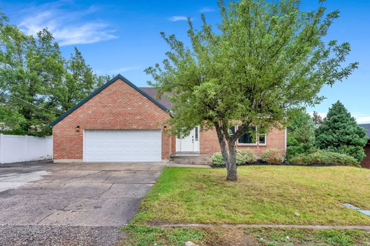Brick exterior with an attached garage, mature tree, and landscaped shrubbery