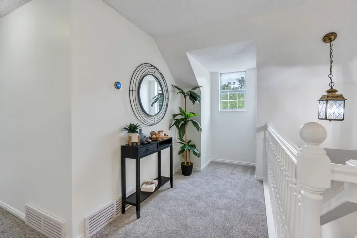 Carpeted landing with a window, white painted walls, white banister, and a decorative pendant light fixture