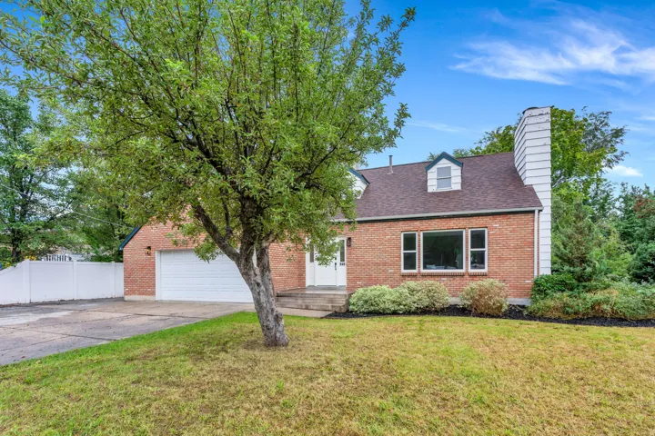 Brick exterior with white trim, attached garage, dormer window, and mature landscaping