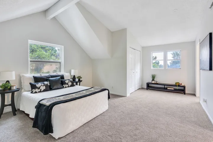 Vaulted ceiling with exposed beams, light gray carpeting, multiple windows, and bi-fold closet doors