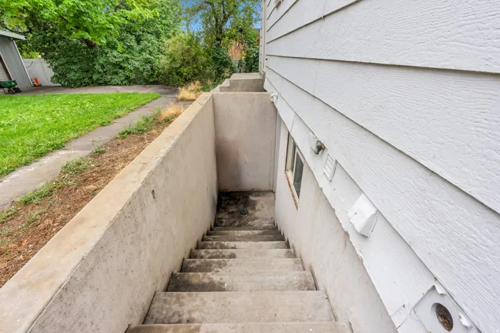 Concrete stairwell entrance with a concrete retaining wall, wood-finish siding, and a grass lawn