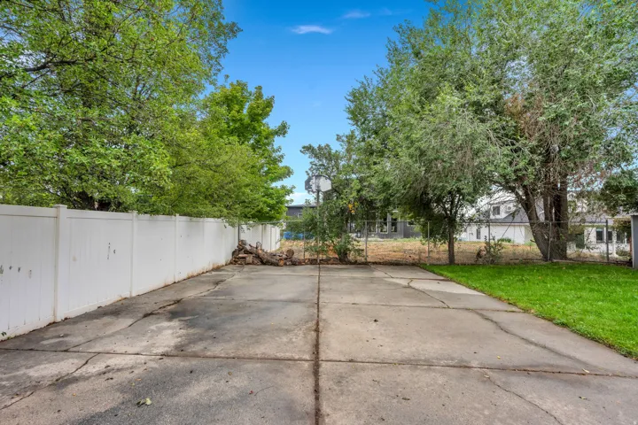 Expansive concrete patio area with a white privacy fence and mature trees