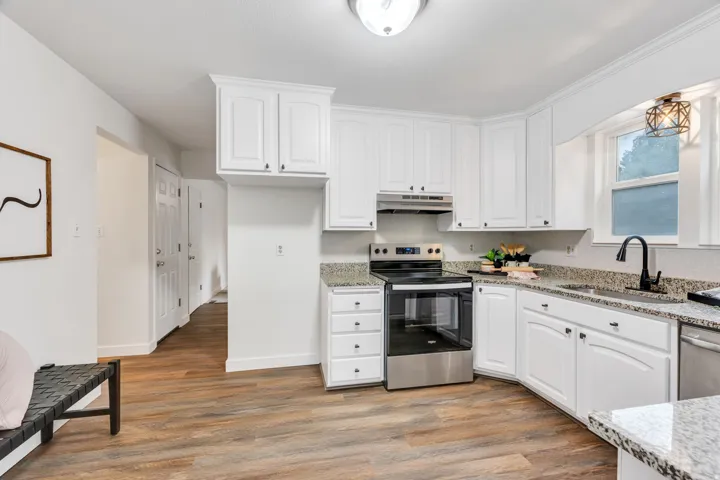 Kitchen featuring white cabinetry, speckled countertops, stainless steel appliances, and wood-finish flooring