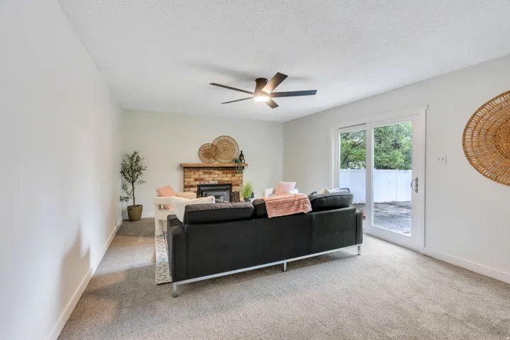 Brick-surround fireplace with wood mantle, ceiling fan with integrated lighting, and sliding glass door