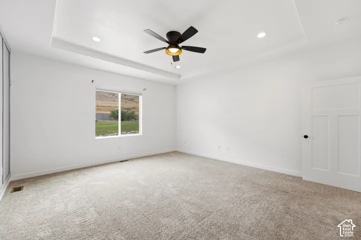Tray ceiling with recessed lighting and a ceiling fan, plush carpet flooring, a multi-pane window, and a white paneled interior door