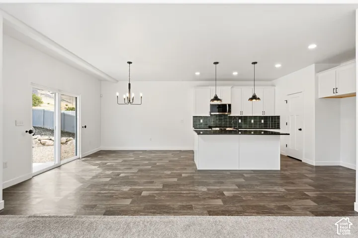 Open-concept living area with wood-finish flooring, white cabinetry, dark tile backsplash, and a kitchen island with pendant lighting