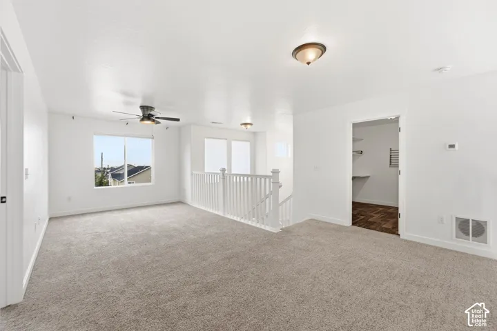 Carpeted room with white walls, a ceiling fan, and multiple windows