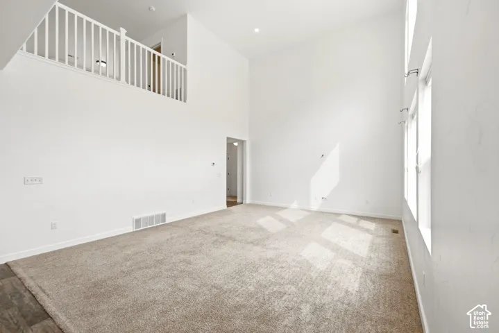 Vaulted ceiling great room with carpet flooring, upper-level railing, and multiple windows