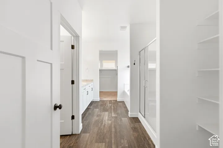 Wood-finish flooring leading to a bathroom featuring a shower with a glass enclosure, white cabinetry, and built-in shelving