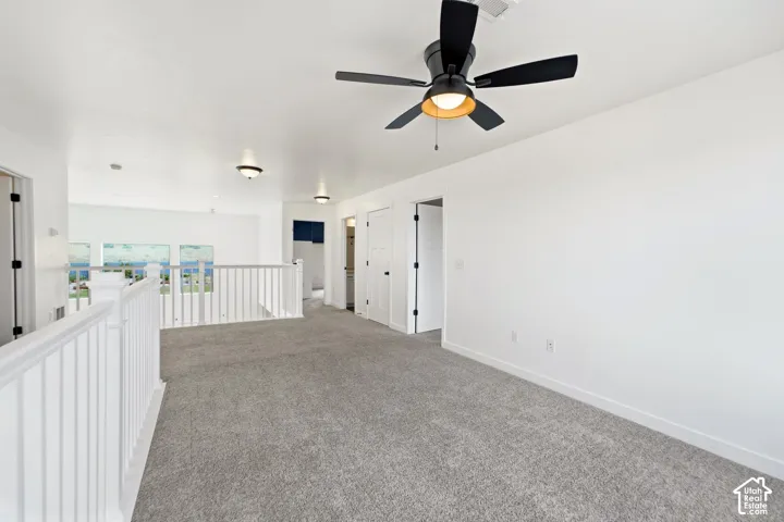 Spacious upper-level room featuring neutral carpeting, recessed lighting, and a ceiling fan with integrated light fixture