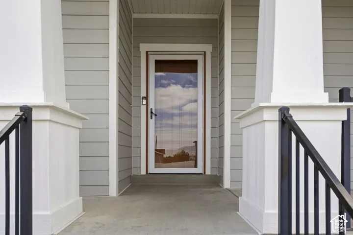 Covered porch with concrete flooring, framed by white pillars, featuring dark metal railings and a wood-finish entry door with a glass storm door