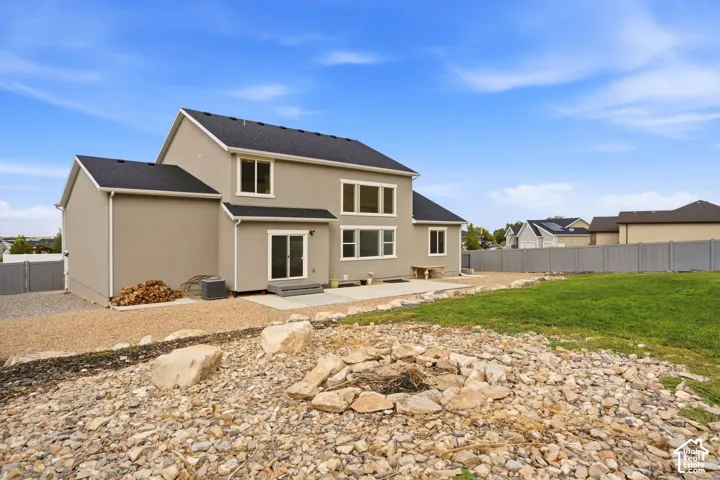 Rear exterior featuring stucco siding, multiple windows, a sliding glass door, a concrete patio, and a landscaped yard with a fire pit