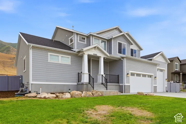 Two-story residence featuring light gray siding, a covered entry porch with white columns, a two-car garage with white doors, and a dark shingle roof