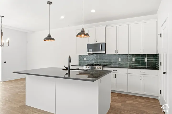 Kitchen featuring a center island with a dark countertop, white cabinetry, dark tile backsplash, stainless steel appliances, and wood-finish flooring