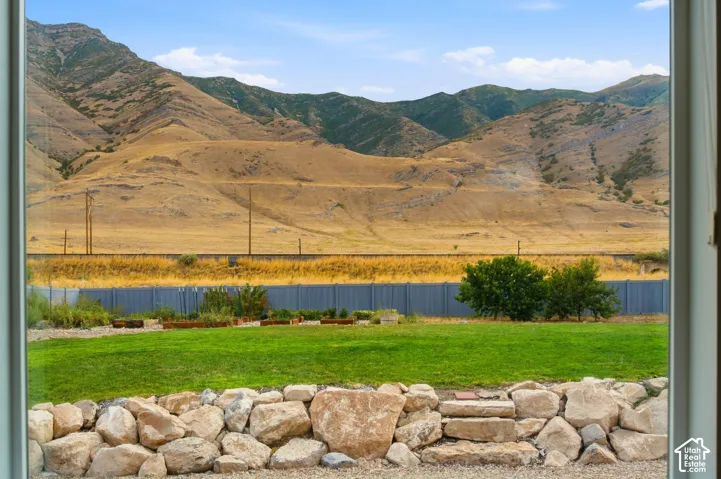 Expansive lawn area featuring a stone retaining wall, raised garden beds, and mature shrubs, set against a mountainous backdrop