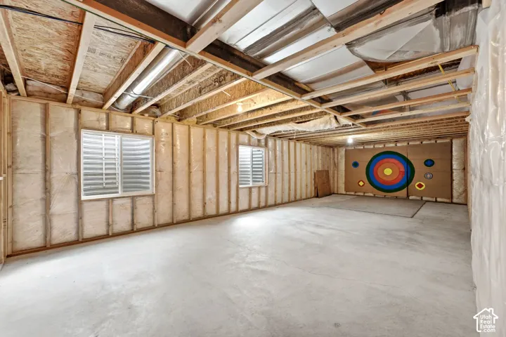 Unfinished basement with concrete flooring, exposed wooden ceiling joists, two windows with blinds, and insulated wall framing