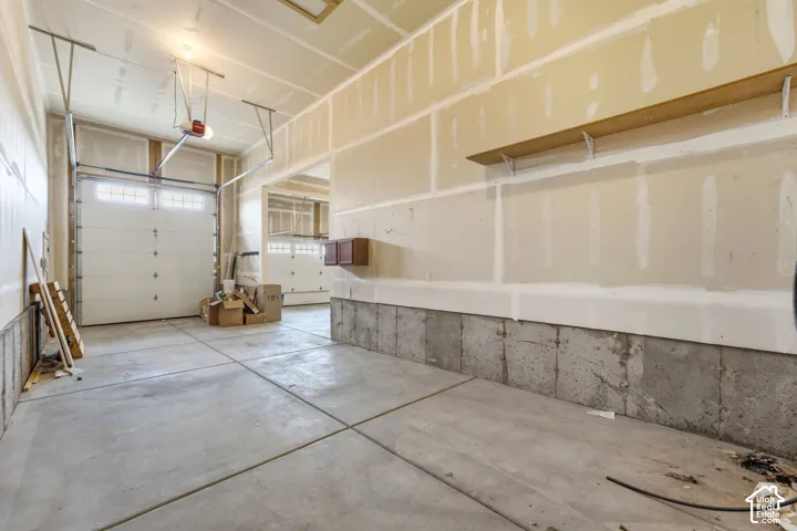 Concrete flooring with multiple garage door bays, overhead door openers, wall-mounted shelving, and built-in cabinetry