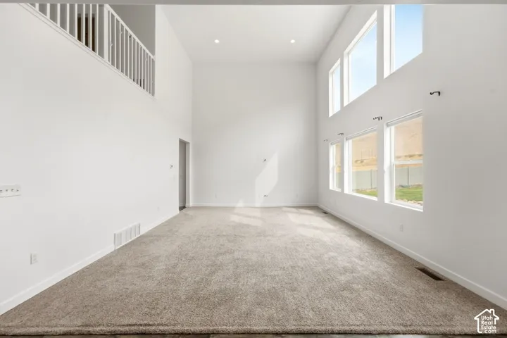 Two-story great room with high ceilings, upper-level balcony, multiple large windows, recessed lighting, and neutral carpeting