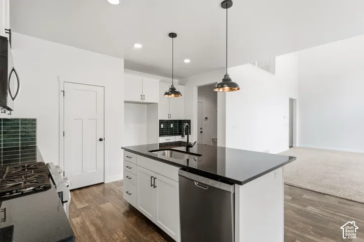 Kitchen with an island featuring a sink, dark countertops, white cabinetry, a built-in dishwasher, and pendant lighting