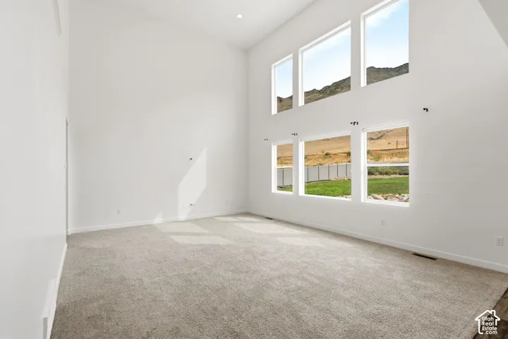 Soaring vaulted ceiling, expansive window array, recessed lighting, neutral carpeting, and a mountain landscape backdrop