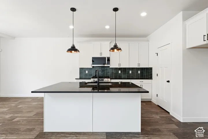 Kitchen featuring a central island with a dark countertop, white cabinetry, dark subway tile backsplash, and wood-finish flooring