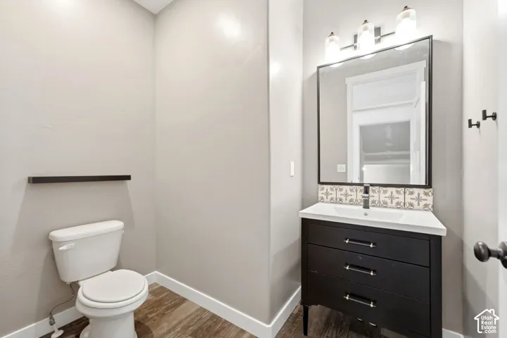 Vanity with an integrated sink, decorative tile backsplash, wood-finish flooring, and wall-mounted lighting