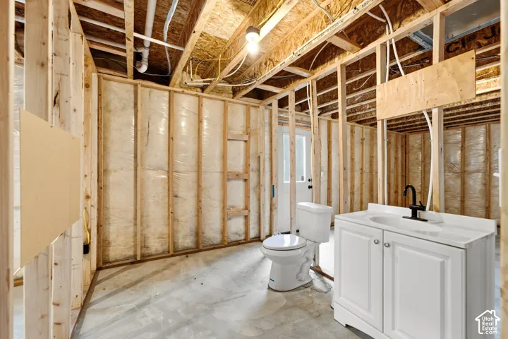 Unfinished basement with exposed wood framing, concrete flooring, and an installed white vanity with a black faucet