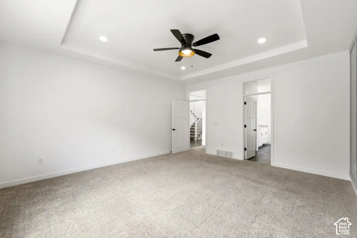 Tray ceiling with recessed lighting and a ceiling fan, neutral carpeting, and white interior doors